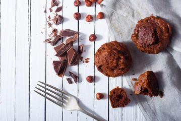 broken chocolate muffin and hazelnuts, fork on white wood table