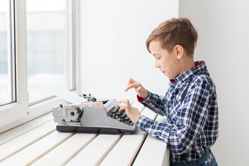 people, children and style concept - young boy with old black typewriter on white background