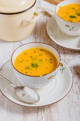 Cup with pumpkin soup and parsley with pieces of pumpkin on the white table