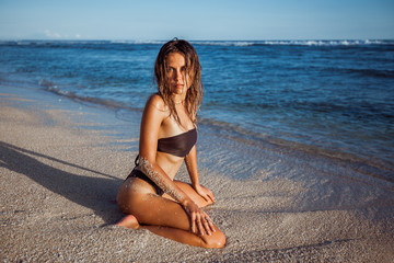 Fototapeta na wymiar Sexy girl in swimsuit sitting on her knees on the beach