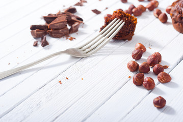 broken chocolate muffin and hazelnuts, fork on white wood table