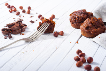 broken chocolate muffin and hazelnuts, fork on white wood table