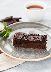 Chocolate cake slice on a gray plate with a cup of tea
