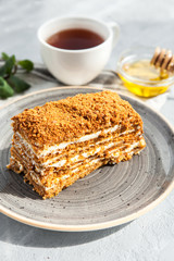 Multi-layered honey cake with sour cream on a gray plate with a cup of tea