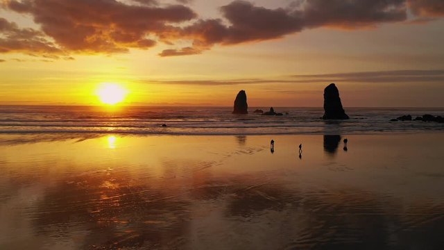 People Walk Cannon Beach as Pacific Ocean Waves Reflect Sunset Glow