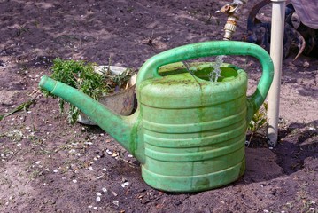 faucet pours water into a green dirty plastic watering can on the ground