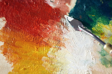 Palette of wood on which a palette knife applied oil paint yellow, red, green and white.