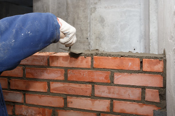Hand with a trowel, in the process of laying a wall of red brick.