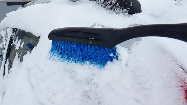 man brushing the car from the snow in winter