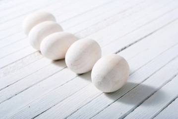white painted wooden eggs on bright wood table background
