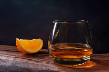 Elegant glass of brandy on black wooden background in warm relaxation atmosphere 