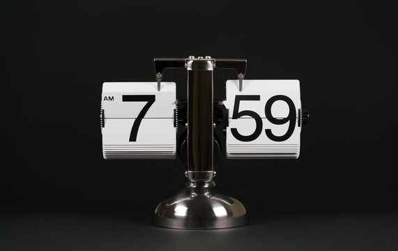 Isolated vintage flip clock on black background at seven o'clock and fifty nine minutes