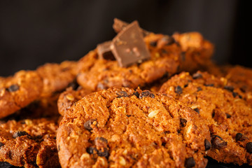 Chocolate chip cookies on rustic dark black background. Stacked chocolate chip cookies on brown napkin. Symbolic image with place for text. Freshly baked. Concept for a tasty snack. Sweet dessert. 