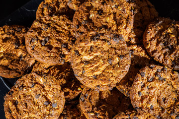 Chocolate chip cookies on rustic dark black background. Stacked chocolate chip cookies on brown napkin. Symbolic image with place for text. Freshly baked. Concept for a tasty snack. Sweet dessert. 