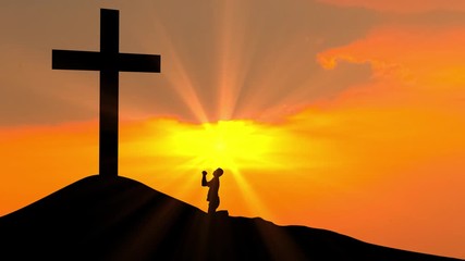 Silhouette of man kneeling and praying to the cross on the hill at sunset time. Shot in 4k resolution