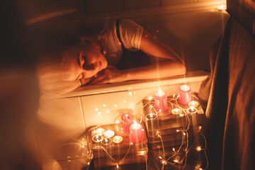 Red candles burning, Christmas lights and garland in bathroom on back bath. Romantic , Valentine's day. Attractive woman relax in bath