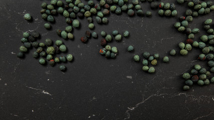Top down view, Black pepper (Piper nigrum) spice spilled on dark working board. Turkish green / blue peppercorn variant.