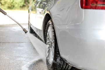 Side, and rear wheel of silver car washed in self serve carwash, water spraying from high pressure...