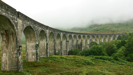 Fototapeta na wymiar Glenfinnan Viaduct (location from Harry Potter movie) on overcast day, fog covering hills in background.