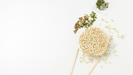 Overhead view of raw instant Asian egg noodles, seasonings and chopsticks on white background