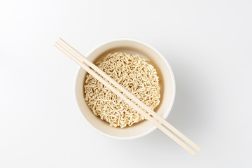 Overhead view of bowl with raw instant Asian egg noodles and chopsticks on white background