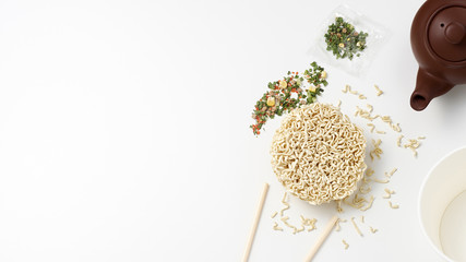 Overhead view of instant noodles, seasonings, chopsticks and teapot on white background