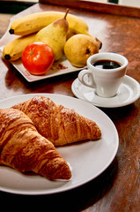 Coffee and croissant breakfast on a vintage wooden table. Espresso, croissants, and fruits. 