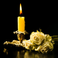 Withered roses, and a burning candle on a black background with reflection