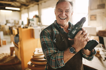 Smiling senior carpenter holding drill machine - Powered by Adobe