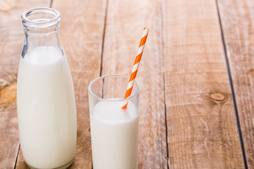 Bottle and glass of milk with straw on wooden table
