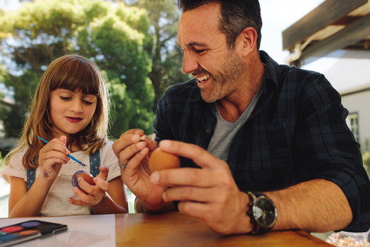 Smiling man sitting with his daughter painting easter eggs