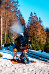 Couple men and woman at Harz steam train during winter in snow landscape, historic steam train in...