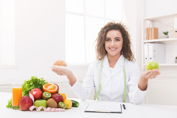 Woman nutritionist holding fruit and croissant in hands