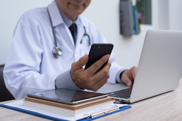 Doctor using smartphone and working on laptop computer