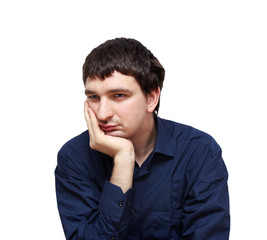 Sad young man in dark blue shirt sitting and propping his head by hand. Isolated on white.