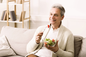 Mature man enjoying healthy salad, relaxing at home