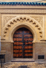 Traditional Moroccan style design of an ancient wooden entry door. In the old Medina of Marrakech, Morocco. Typical, old, brown intricately carved, studded, Moroccan riad door