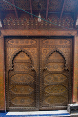 Traditional Moroccan style design of an ancient wooden entry door. In the old Medina of Marrakech, Morocco. Typical, old, brown intricately carved, studded, Moroccan riad door