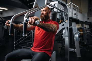 Fototapeta na wymiar Muscular athlete on exercise machine in gym