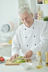 Portrait of elderly male chef cutting cabbage at kitchen
