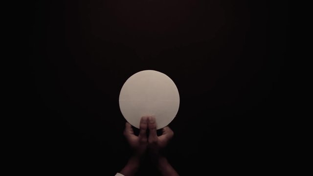 Pastor hands raising a communion bread on dark background. Shot in 4k resolution