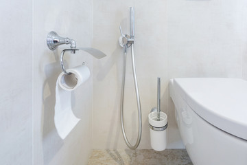 toilet and detail of a corner shower bidet with toilet paper holder on wall mount shower attachment