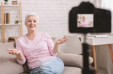Friendly senior woman vlogger sitting on sofa dating online