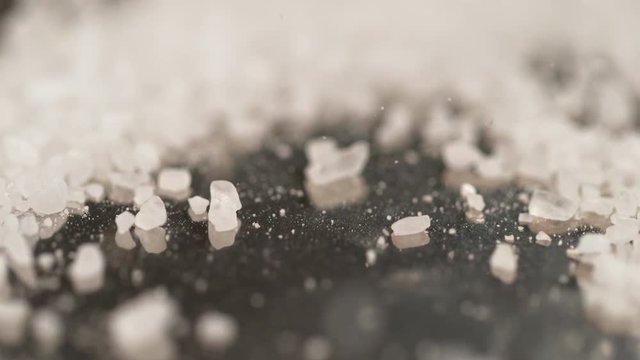 SLOW MOTION, MACRO, DOF: Pristine white salt crystals are sprinkled across the black surface of the chef's table. Cool shot of sugar crystals fall and bounce around the granite kitchen countertop.