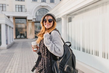 Laughing girl with black backpack walking around city and drinking coffee in good day. Outdoor...