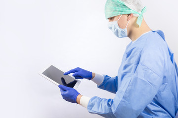 Surgeon doctor in sterile gloves preparing for operation using tablet computer. He is wearing...