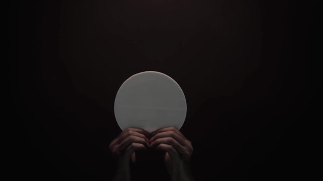 Priest hands raising a communion bread on dark background. Shot in 4k resolution