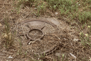 Old rusty manhole of a well among grass of a dry lawn