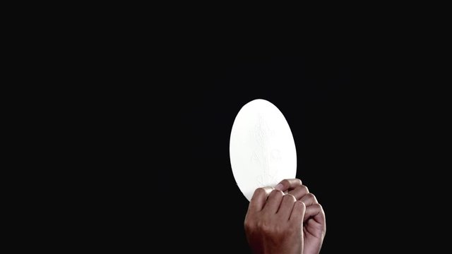 Priest hands raising a sacramental bread or communion bread on dark background. Shot in 4k resolution