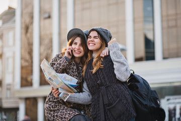 Portrait fashionable smiling girls expressing brightful emotions on sunny day in city. Happy travelling together, lovely moments of joyful toutists, stylish, enjoying vacation, talking on the phone